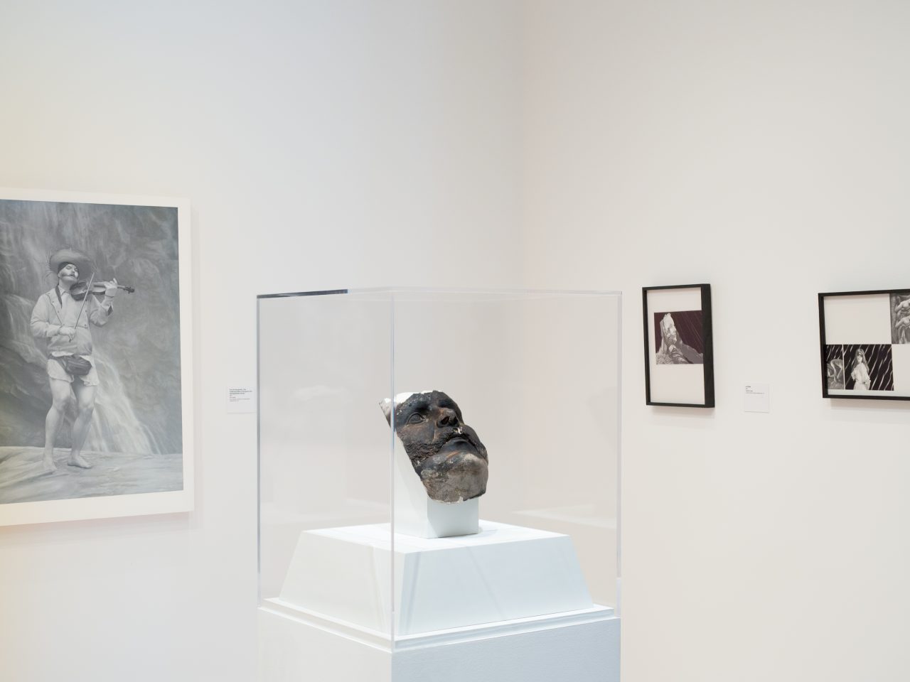 A stone mask enclosed in glass surrounded by three drawings on the walls behind it