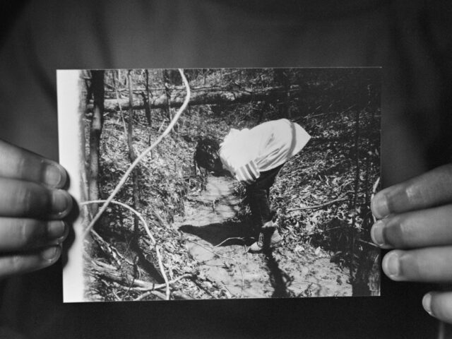 black and white image of a little girl bending down and looking in the woods