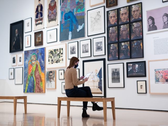 A person sits in a gallery surrounded by works from the MSU Broad Art Museum permanent collection.