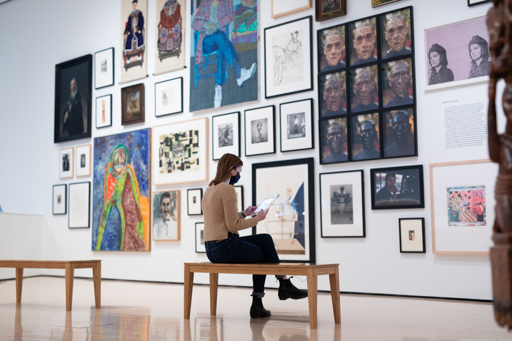 A person sits in a gallery surrounded by works from the MSU Broad Art Museum permanent collection.