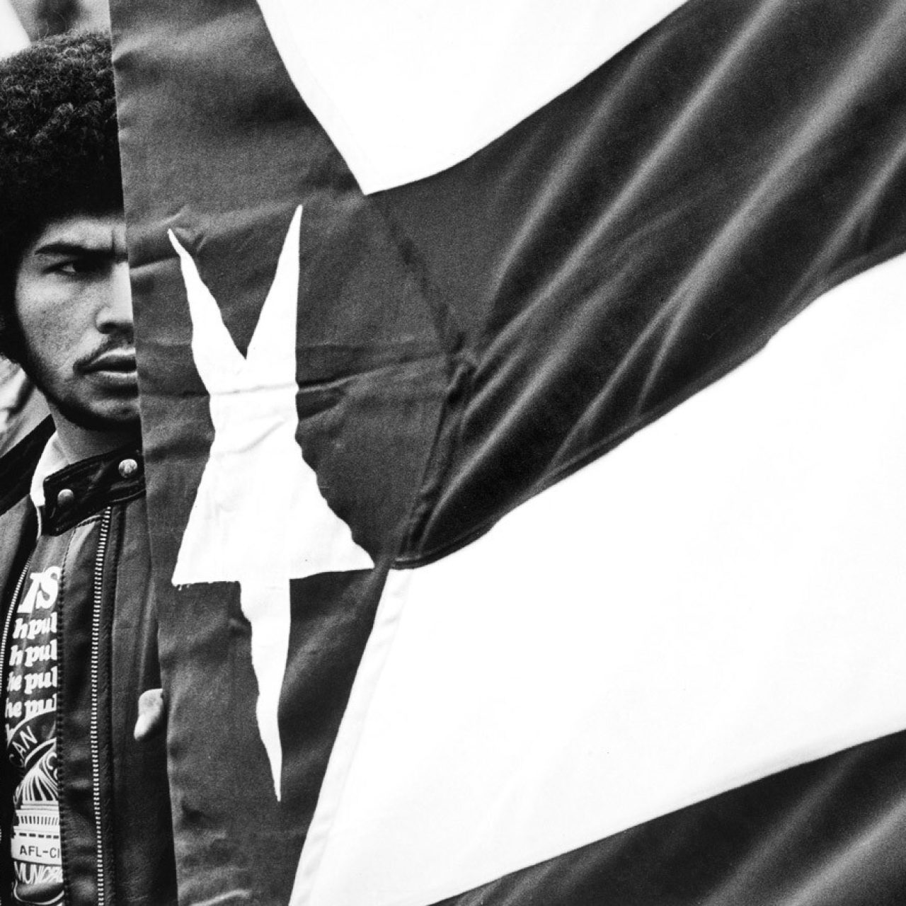 Black and white photograph of a man next to Puerto Rican flag.