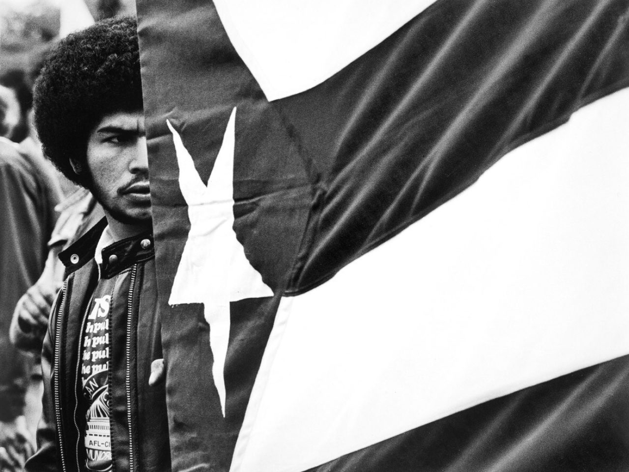 Black and white photograph of a man next to Puerto Rican flag.