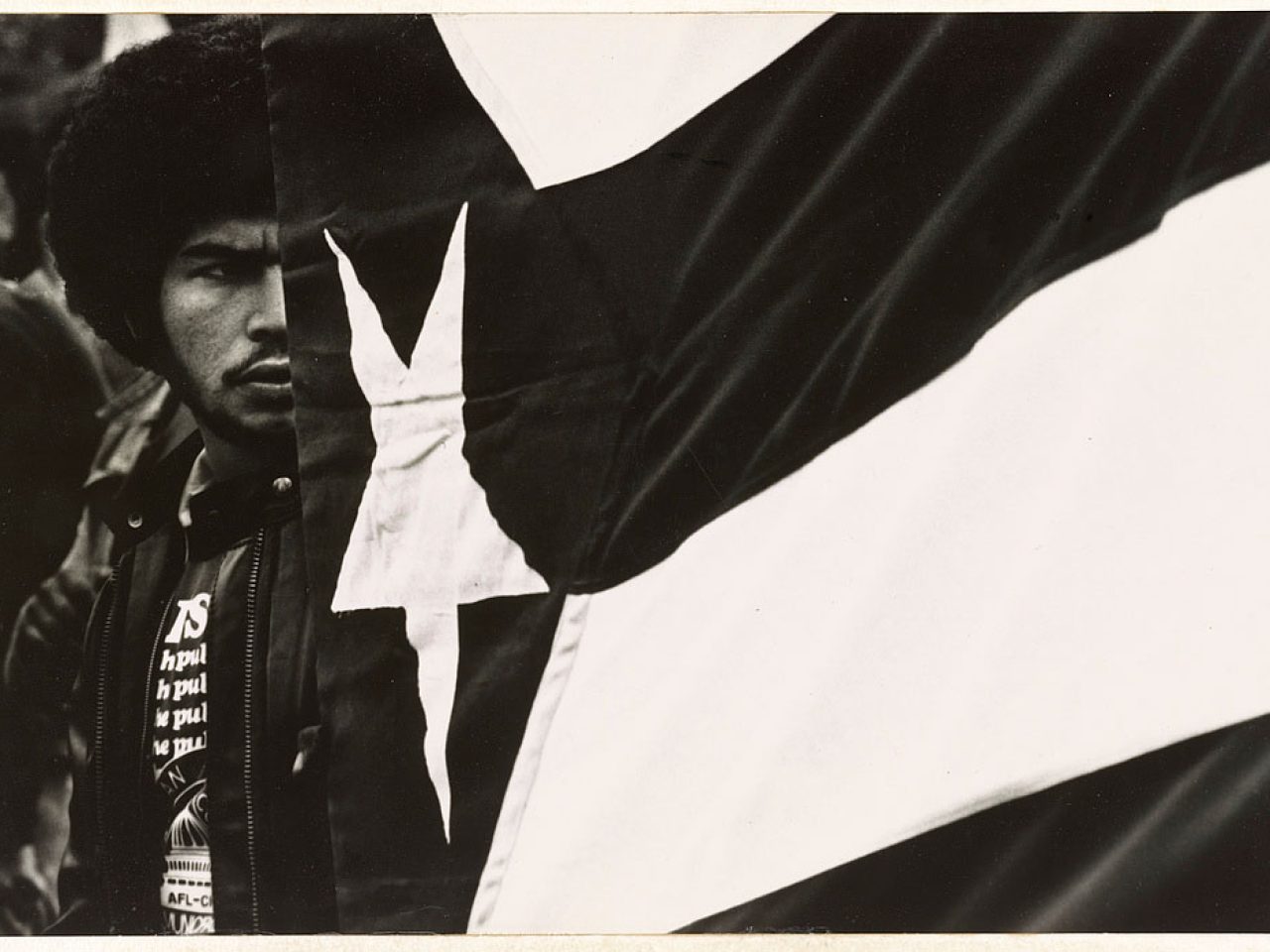 Black and white photograph of a man next to Puerto Rican flag