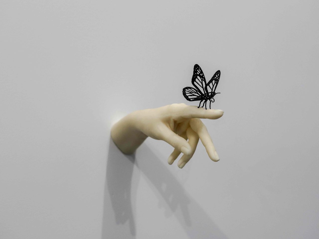 Sculpture of a cream colored hand with black butterfly on finger