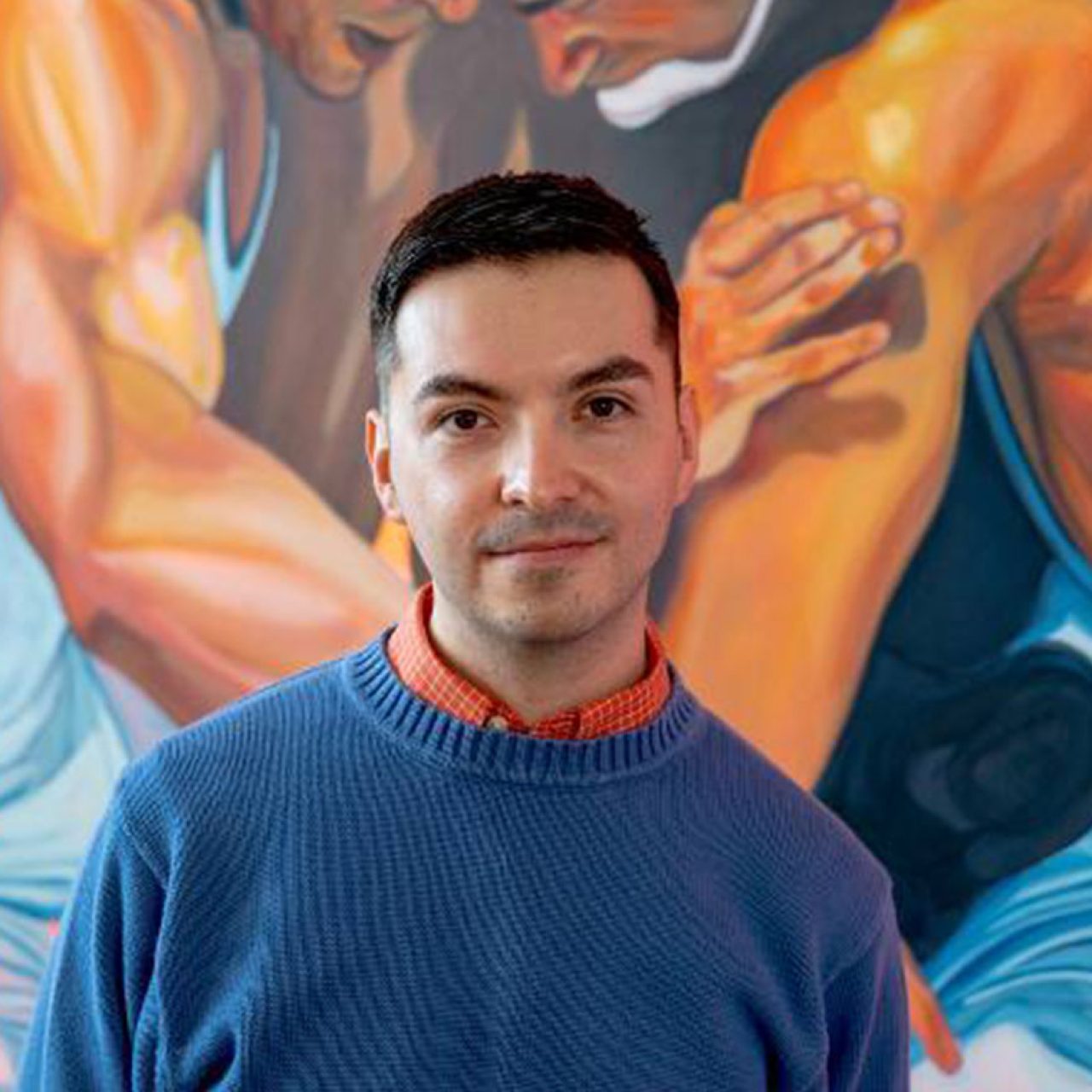 Headshot of artist Gustavo Uriel Ayala, in front of artwork depicting wrestlers